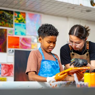 Teacher guiding a young student in painting with vibrant colors in art class.