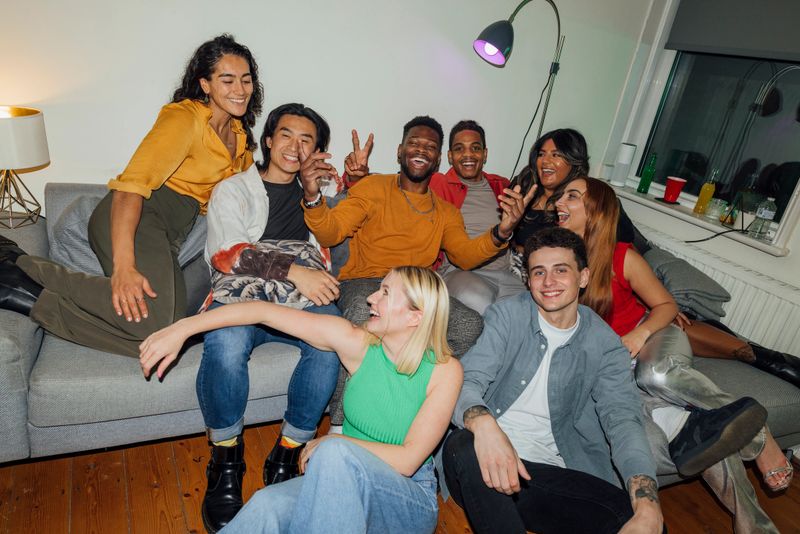 A group of young people enjoying a party at a house in North Shields, North East England. They are all sitting together, smiling and laughing,  some looking at the camera.