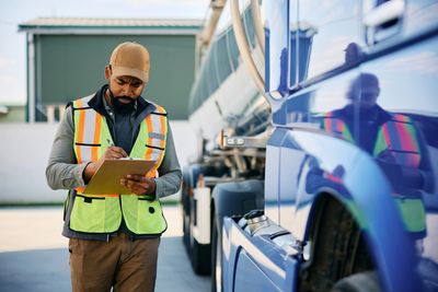 A worker inspecting and taking notes next to a blue truck.