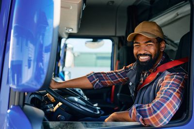 A black truck driver sitting in his blue truck smiling