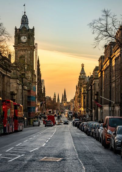 Historic city street with clock tower at sunset and lined with parked cars.