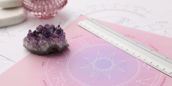 Astrology chart with amethyst crystal, candle, and ruler on pastel background.