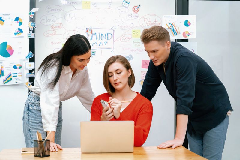 Professional business team working together by using laptop in start up project at meeting in front of glass board with mind map while colleague brainstorm and discuss about strategy. Immaculate.