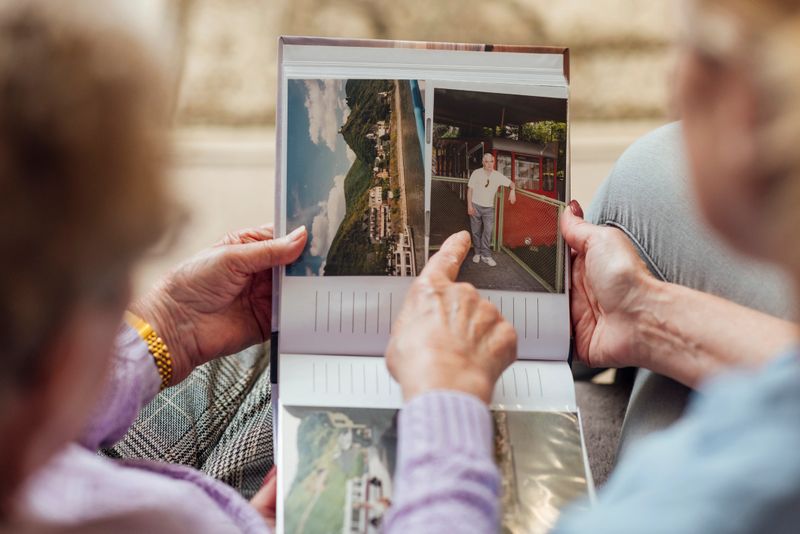A high angle view of an unrecognisable mature woman and her mother looking through a photo album as they sit on a sofa at home in Seghill, Northumberland. The senior woman is staying with her daughter for support and care as she has dementia and they are looking through a photo album together to aid her memory of past relationships and moments in time. The main focus is the photo album and the senior woman is pointing at a picture of her late husband on holiday in a previous year as she is reminded of him.Videos also available for similar scenario.