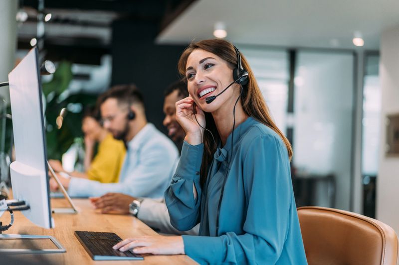 Shot of call center operators working in the office. Female call center agent working with her colleagues in modern office. Smiling beautiful businesswoman working in call center.