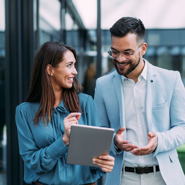 Two professionals happily discussing work using a digital tablet.