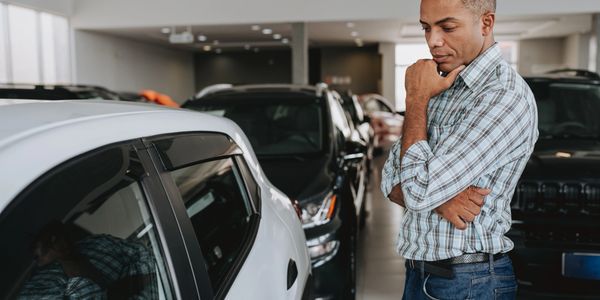 Man thoughtfully inspecting a car inside a showroom.