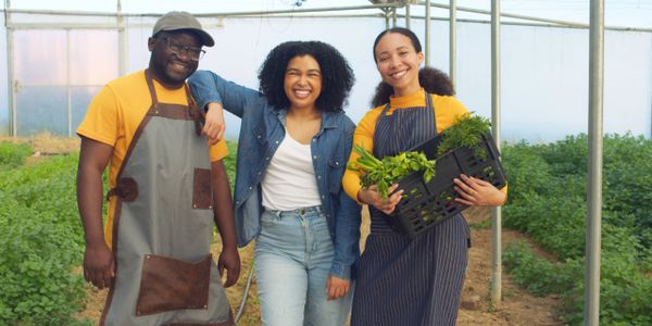 Three happy farmers in a greenhouse with fresh produce.
