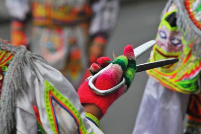 Manos con guantes coloridos sosteniendo una tijera en traje tradicional.