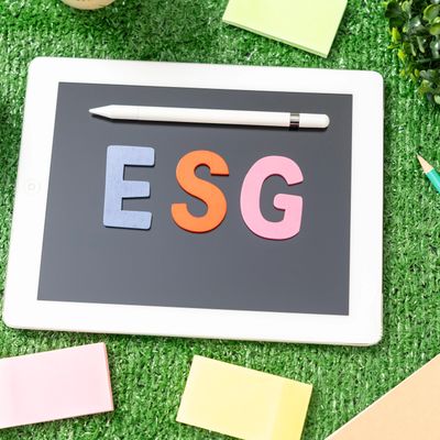 Tablet on grass displaying ESG letters with a stylus and sticky notes around.