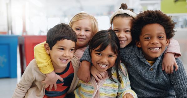 Group of five diverse children smiling and hugging.