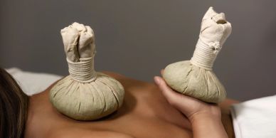 Herbal compress balls used in therapy on a person's back.