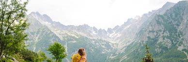 Hiker with yellow backpack enjoys mountain view on rocky trail.