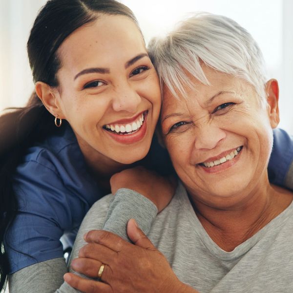 A joyful young woman embraces an elderly woman, both smiling warmly.
