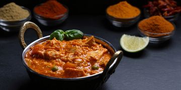 A bowl of rich Indian curry with spices and lime wedge.