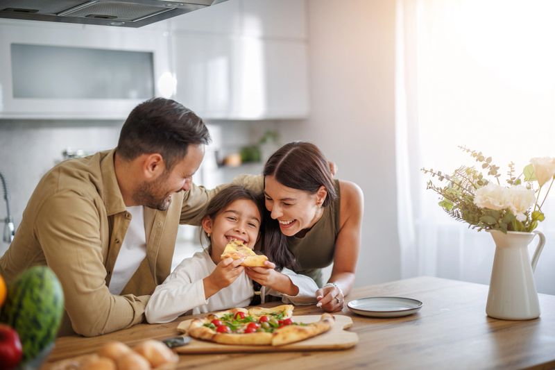Mom, dad and daughter are eating together at home. Happy family eating pizza at home.