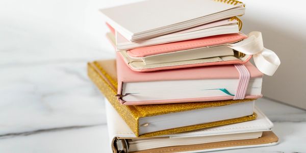 Stack of various colorful notebooks and planners on a marble surface.