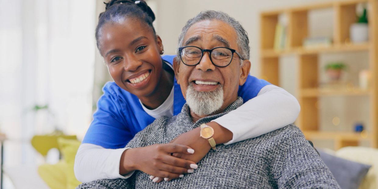A happy caregiver embracing an elderly man.