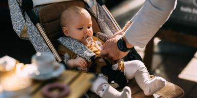 Baby in stroller being fed by an adult.