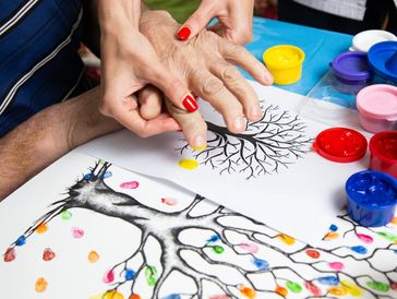 Hands creating colorful fingerprint art on tree drawings.