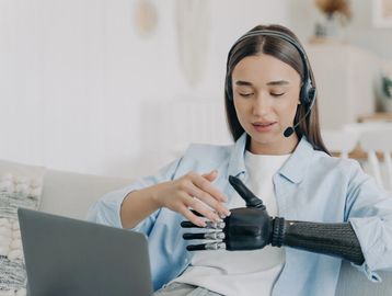 a woman with long brown hair, blue shirt and prosthetic left arm completes a headset call.