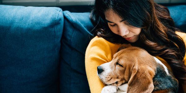 Woman cuddling a sleeping dog on a couch.