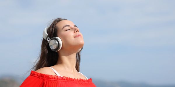 Woman in red dress enjoying music with headphones outdoors.