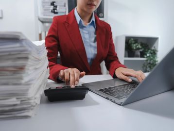 Professional woman using calculator and laptop at work.