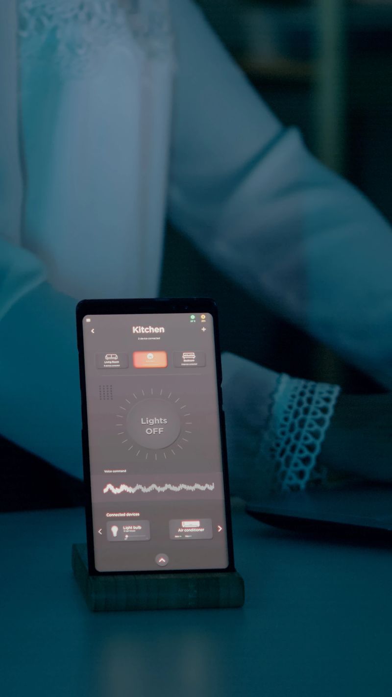 Woman typing at laptop sitting in home with automation lighting system using voice controlled on smartphone turning on bulbs. Speaker gadget responds to commands, person controlling ambiance light
