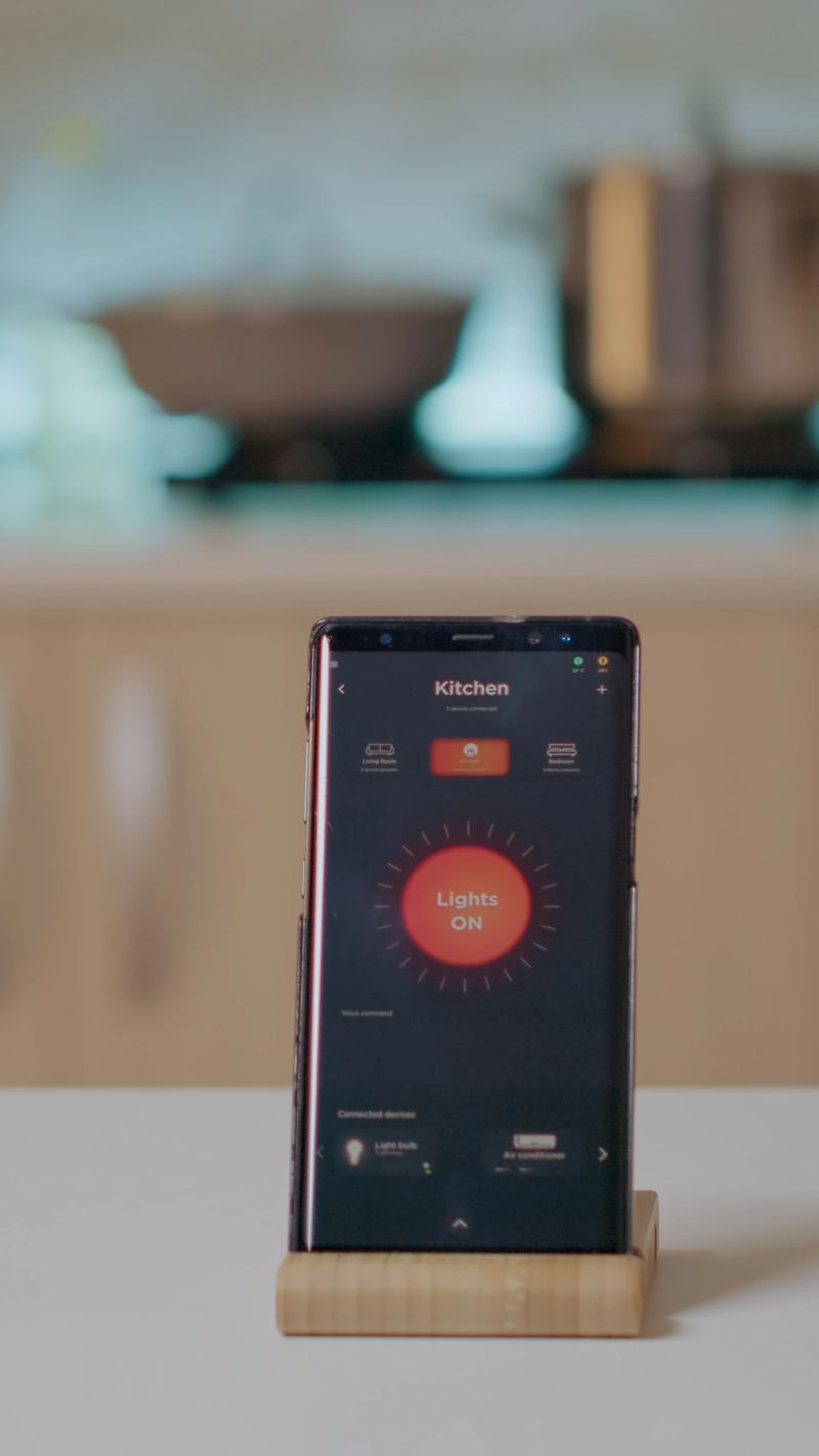Smart home application on phone placed on kitchen desk in empty house automation system, turning on the light. Mobile with wireless lighting controlling, high tech to monitoring electricity effiency