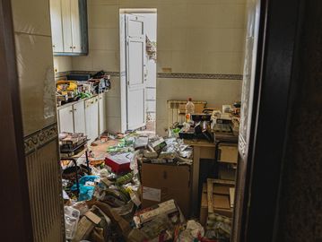Cluttered kitchen filled with various boxes and bags, visible through a doorway.