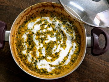 A pot of creamy spinach curry with swirls of cream on top.
