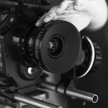A hand adjusting the lens of a professional video camera in low light.