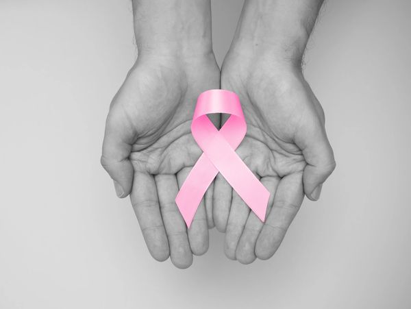 Desaturated photo of two hands holding a pink breast cancer ribbon.