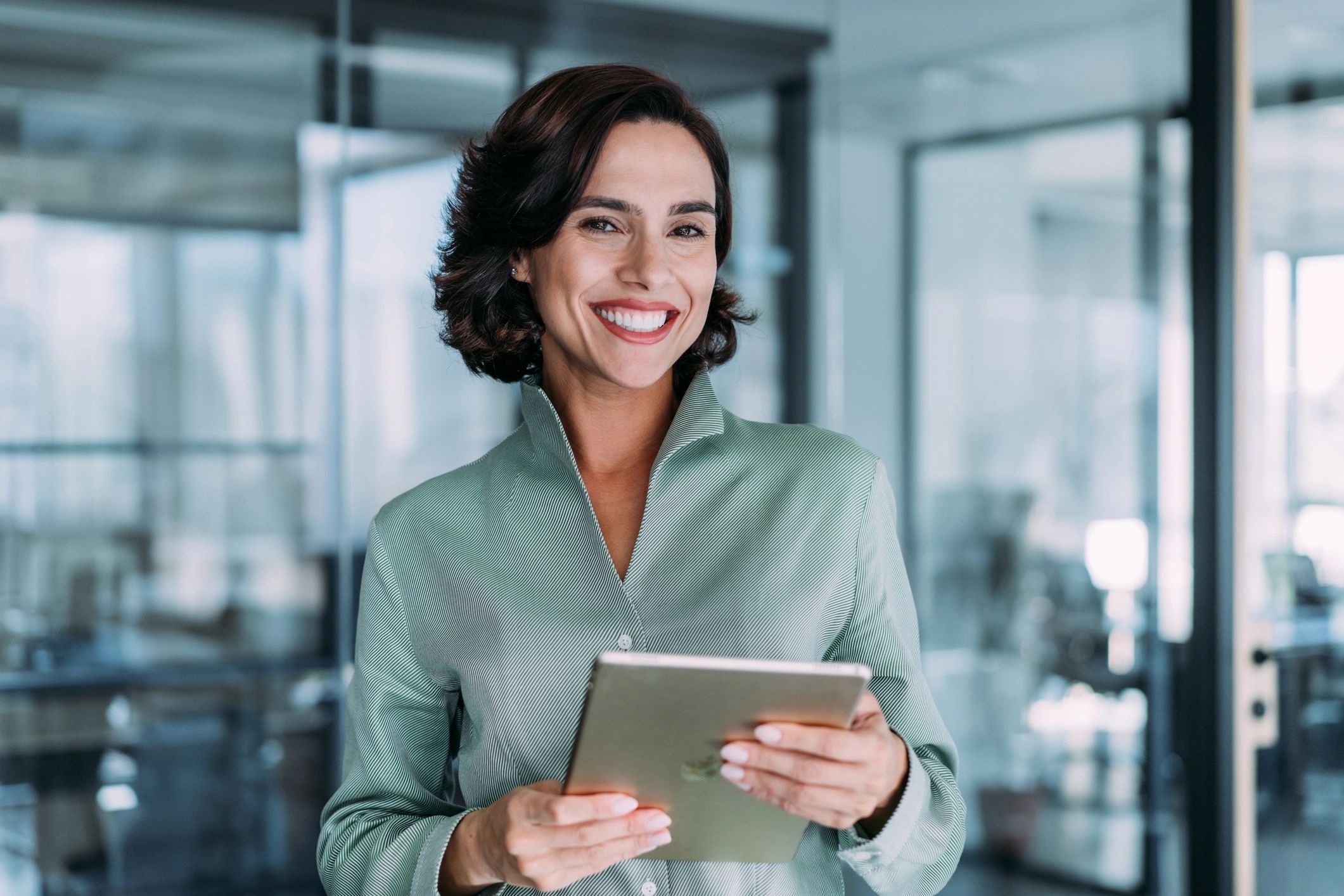 Confident woman smiling while holding a tablet in a modern office.