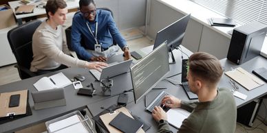 Three coworkers collaborate on coding and laptop tasks in a modern office.