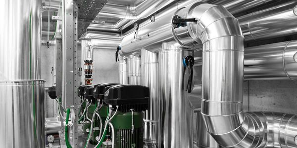 Industrial mechanical room with shiny metal pipes and green machinery.
