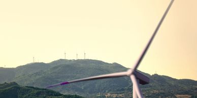 Wind turbines on green hills under a pale sky.