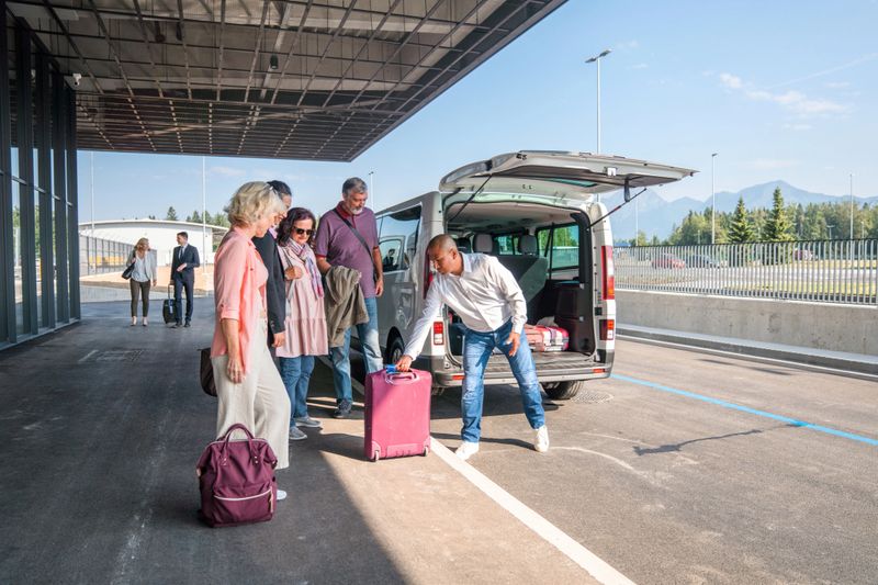 Diverse group of people collecting personal luggage from a airport shuttle van. Standing at the airport departure area.