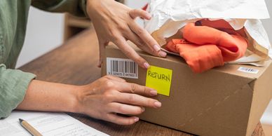 Hands placing a 'RETURN' sticker on a package with clothes inside.