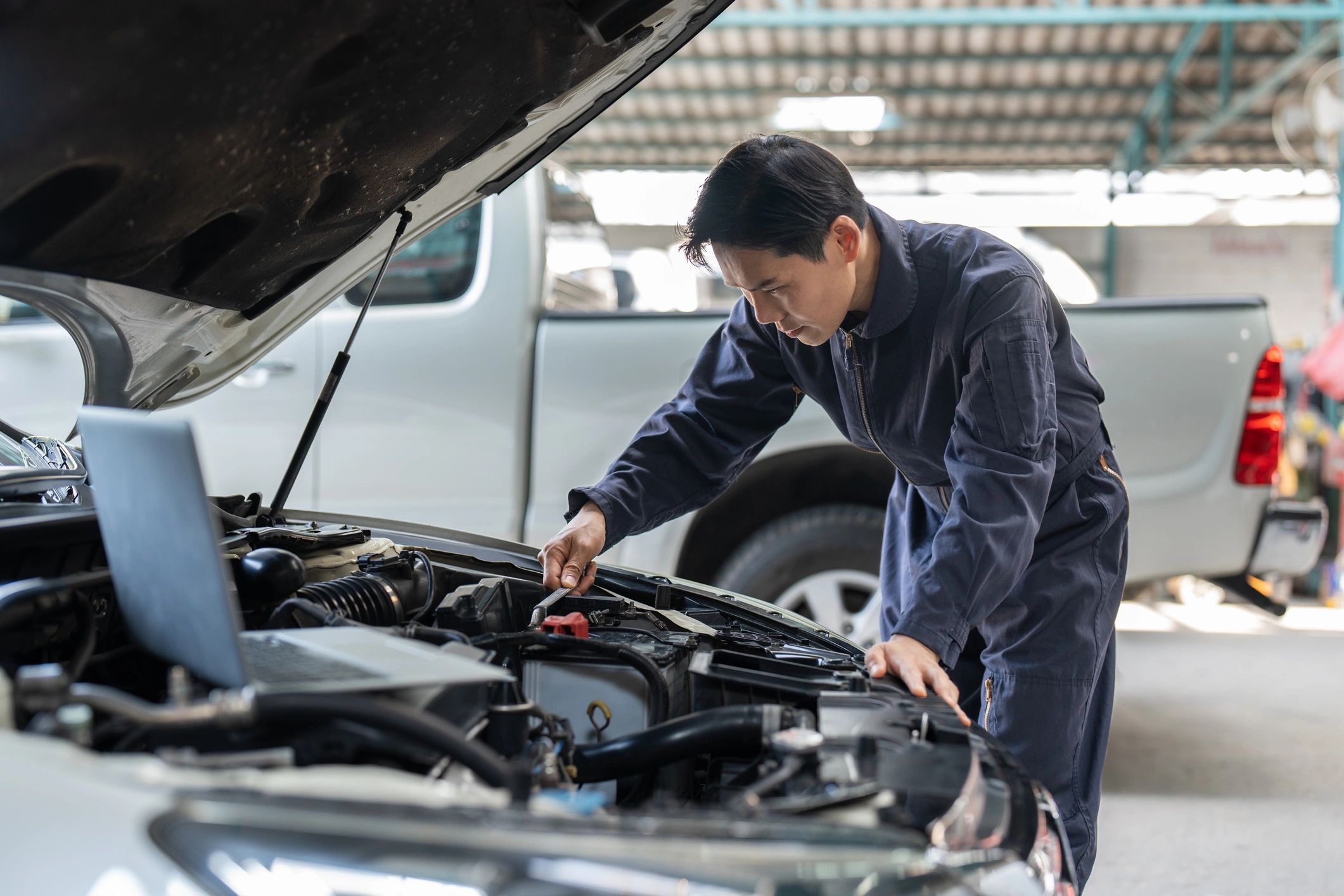 Mechanic inspecting car engine with laptop nearby.