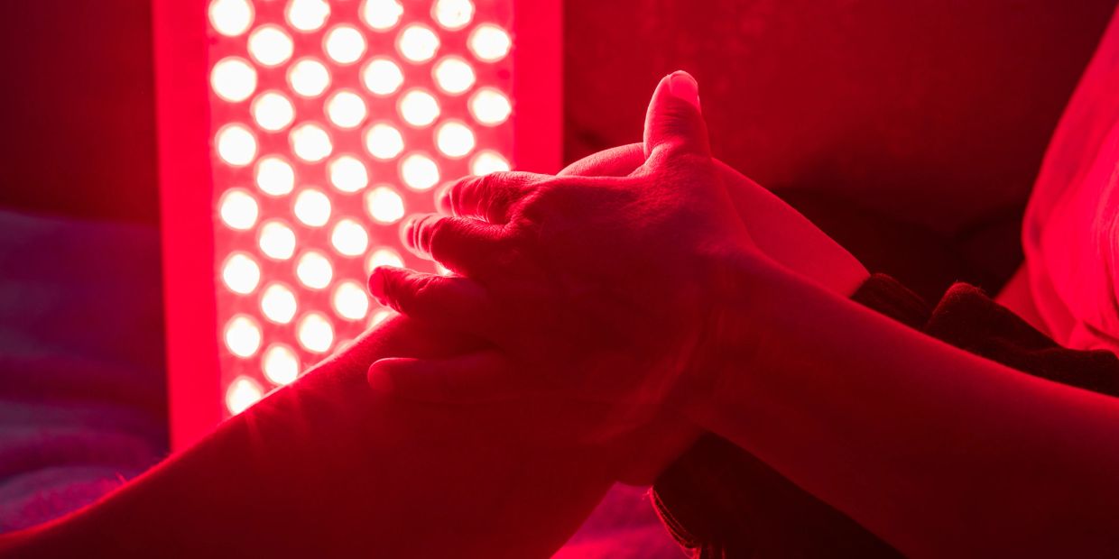 Hands holding a knee near a red light therapy panel.