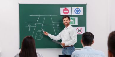 Instructor teaching traffic rules with a road diagram on the chalkboard.