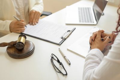 Two people discussing legal documents at a desk with a gavel and laptop.
