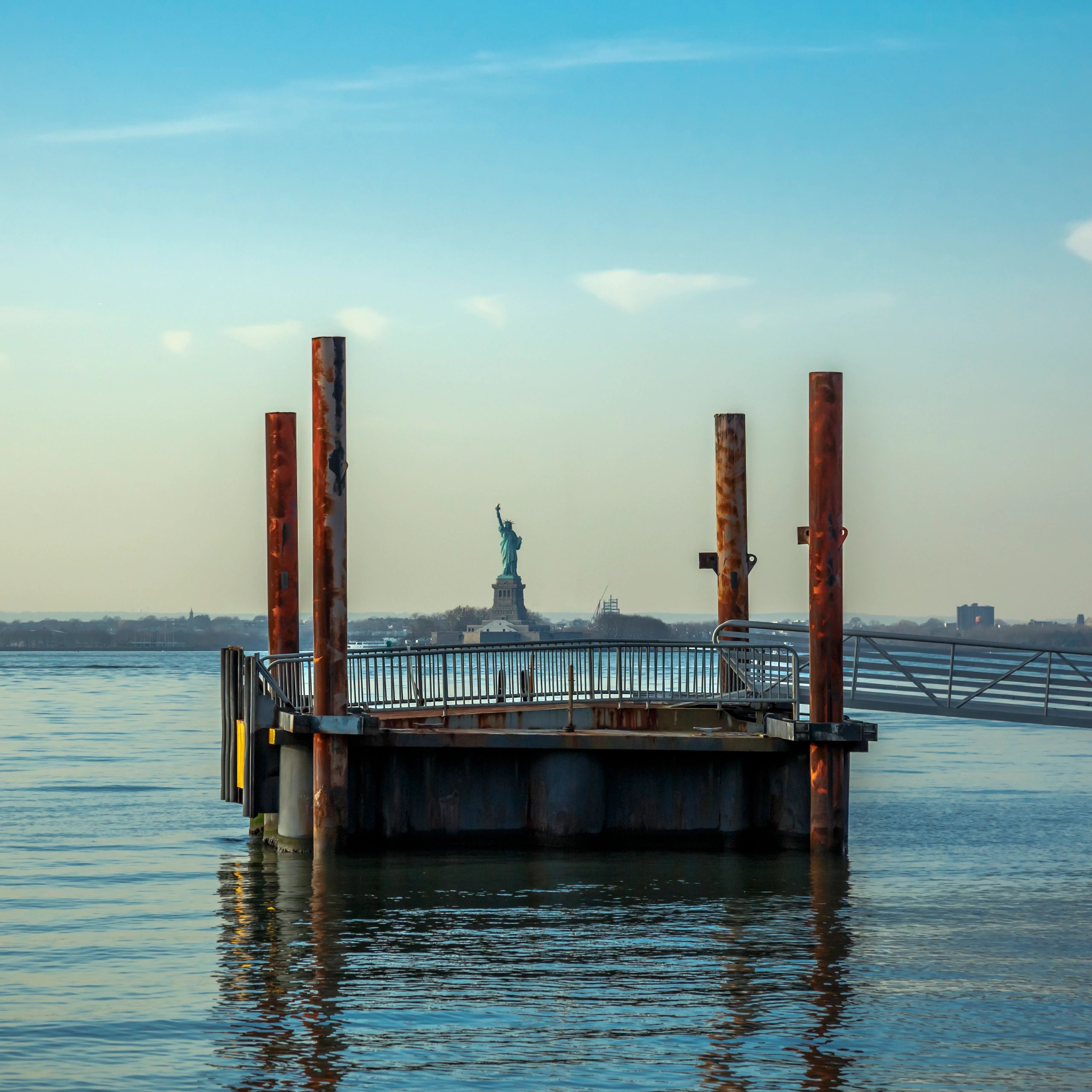 Rusty pillars on a pier with the Statue of Liberty in the background.