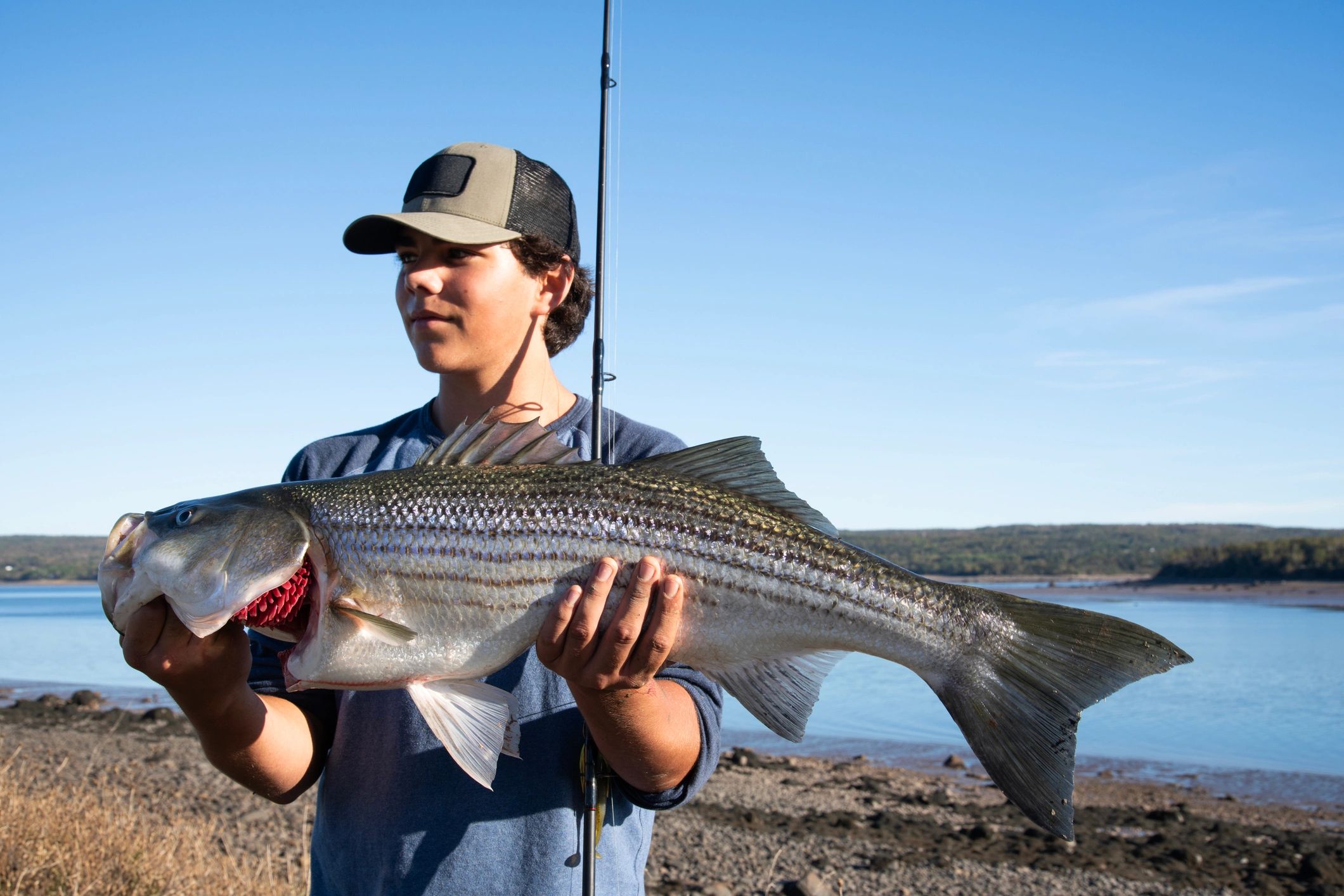 Young man holding a large fish by the water.