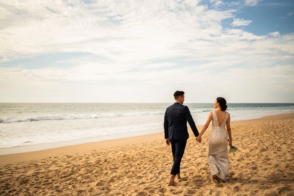 A couple in wedding attire walking hand-in-hand on a beach.