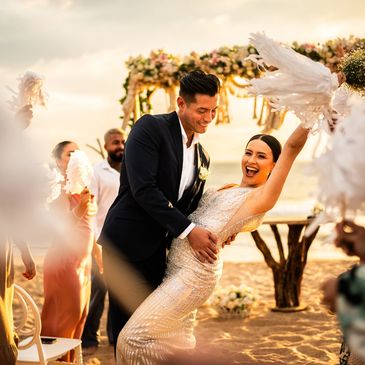 A joyful couple celebrating their wedding on a beach at sunset.