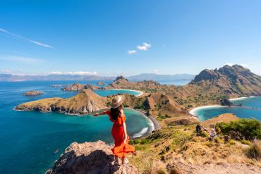 A woman in a red dress overlooking a scenic island landscape with blue waters.