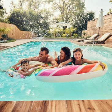 A family enjoys playful moments in a sunny backyard pool with colorful floaties.